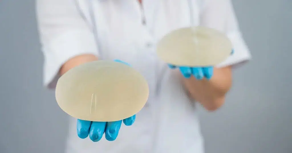 Gloved medical professional holding out two silicone breast implants for shape comparison