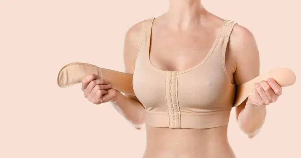 Woman wearing a beige post-surgical bra and holding compression straps, representing breast reduction recovery care.