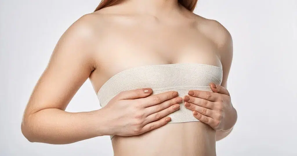 Woman with compression bandage over chest holding breasts, showing post-surgical care and swelling after breast reduction.