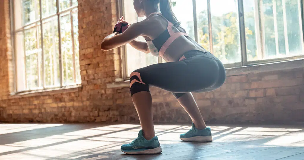 Woman performing squats in a sunlit gym studio, demonstrating glute-strengthening exercises commonly recommended to improve the appearance of a sagging butt.