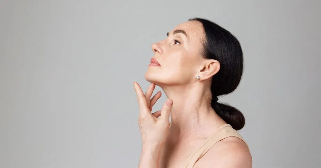 Mature woman looking upward and touching her chin, suggesting consideration of combining chin liposuction with other cosmetic procedures.