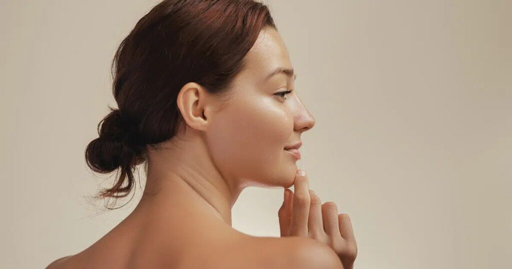 Woman with hair tied back gently touching her chin, symbolizing healing process after chin liposuction recovery.