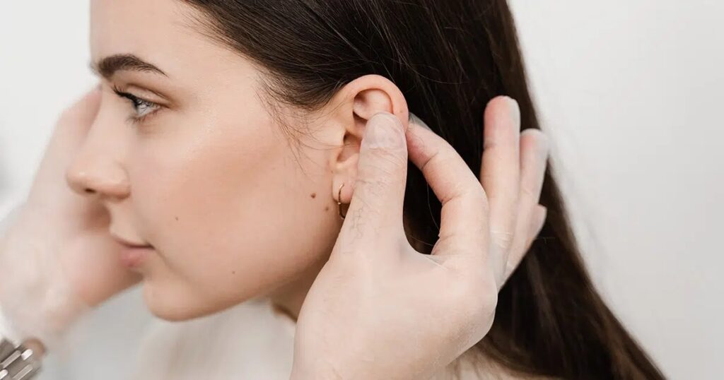 Close-up of a medical professional examining a woman's ear, illustrating consultation for otoplasty or ear reshaping surgery.