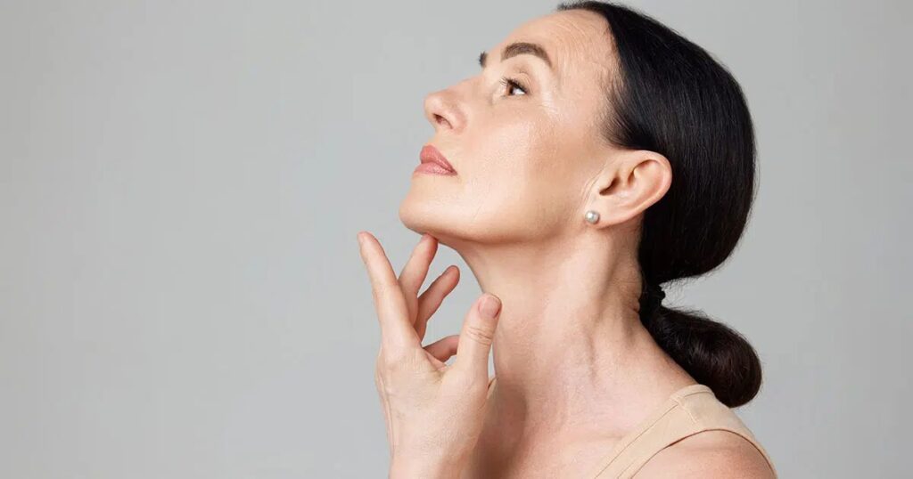Mature woman gently examining her jawline and neck, highlighting smooth skin and refined contours during mini facelift recovery.