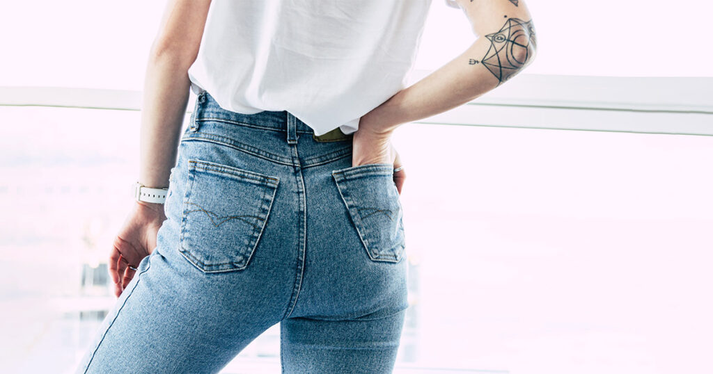 Rear view of a woman wearing high-waisted jeans, illustrating the flat or deflated buttock contour commonly referred to as "mom butt," often caused by aging, weight changes, or postpartum body shifts.