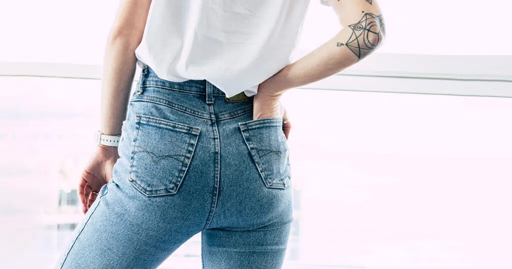 Rear view of a woman wearing high-waisted jeans, illustrating the flat or deflated buttock contour commonly referred to as "mom butt," often caused by aging, weight changes, or postpartum body shifts.
