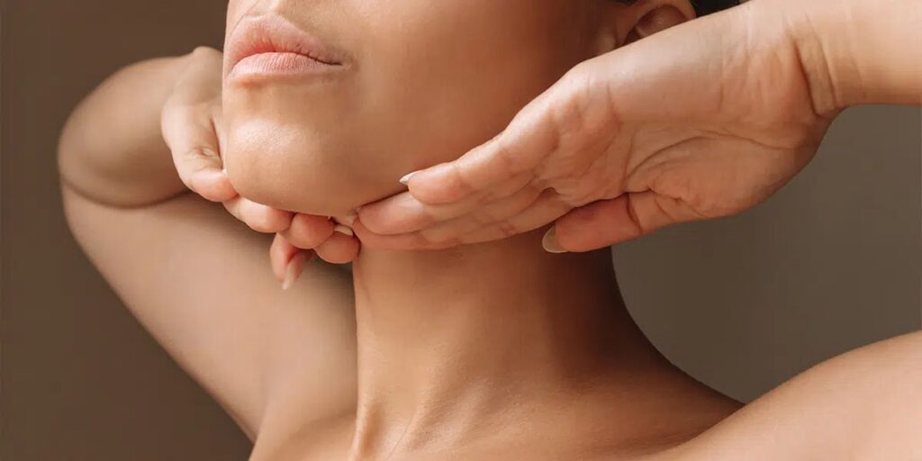 Woman gently lifting the skin under her chin with both hands, illustrating concerns about neck contour and potential areas for neck lift scars.