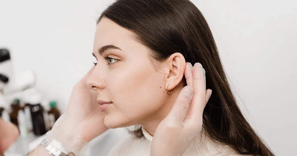 Medical professional gently examining a woman’s ear during a follow-up appointment, illustrating the recovery process after otoplasty surgery.