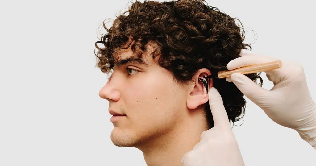 Medical professional examining a young man's ear with a surgical tool, illustrating pre or post-operative assessment for otoplasty, a procedure that typically provides permanent ear reshaping results.