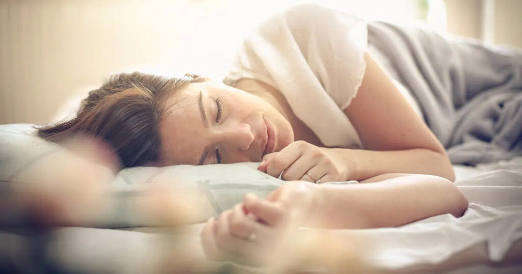 Woman resting on her side in a well-lit bedroom, illustrating post-surgery sleep position for lipo 360 recovery.