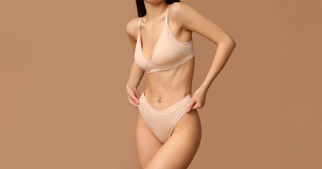 Woman in nude undergarments revealing a narrow breast base and downward-pointing shape, illustrating characteristics often associated with tubular breasts—a condition treated through breast revision surgery.