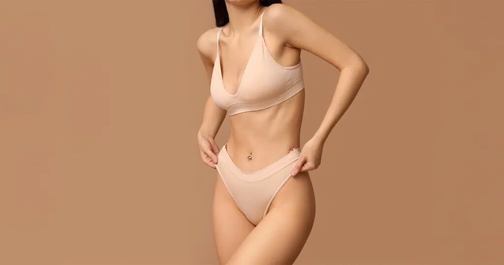 Woman in nude undergarments revealing a narrow breast base and downward-pointing shape, illustrating characteristics often associated with tubular breasts—a condition treated through breast revision surgery.