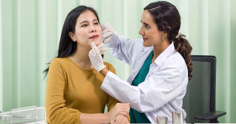 Medical professional examining a female patient’s face during a consultation, representing pre-procedure evaluation for facial fat transfer or volume restoration treatments.