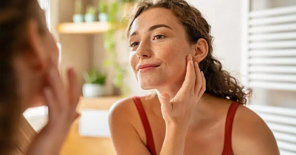 Woman examining her youthful, smooth skin in the mirror, showcasing natural results after fat transfer to the face procedure.