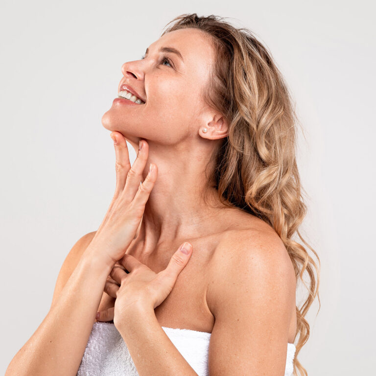 Woman wrapped in a white towel tilting her head back, fingers along her jaw and collarbone