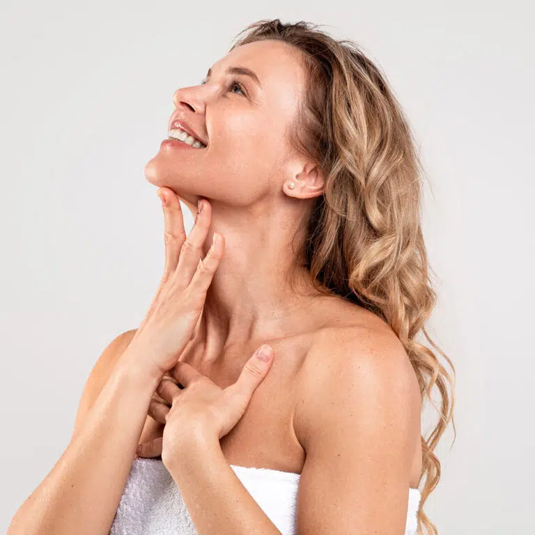 Woman wrapped in a white towel tilting her head back, fingers along her jaw and collarbone