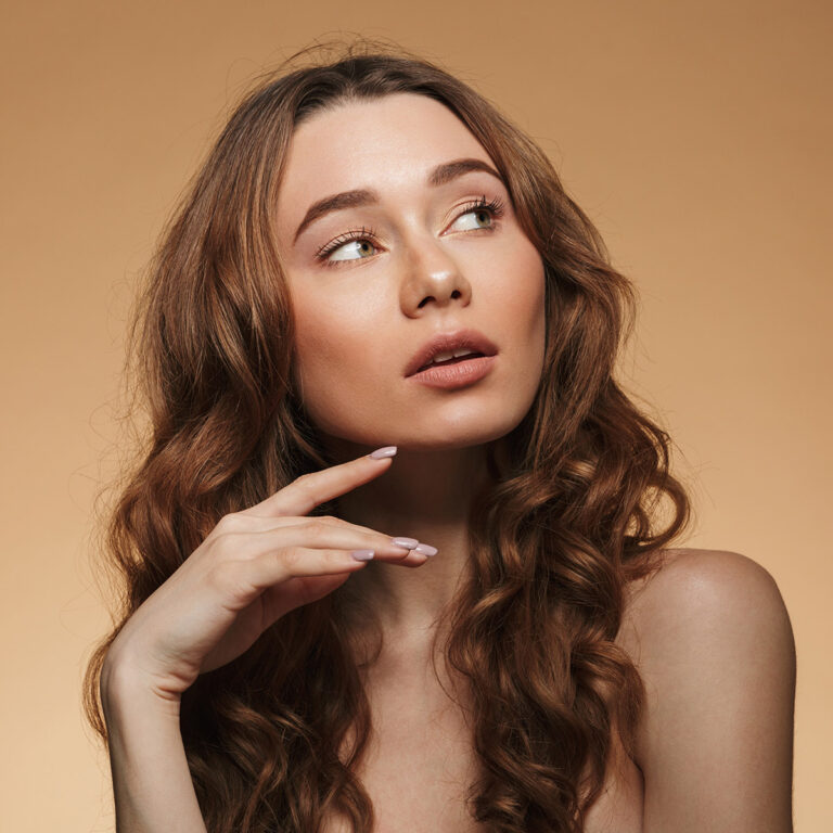 Woman with long wavy hair and bare shoulders resting her fingertips just below her chin