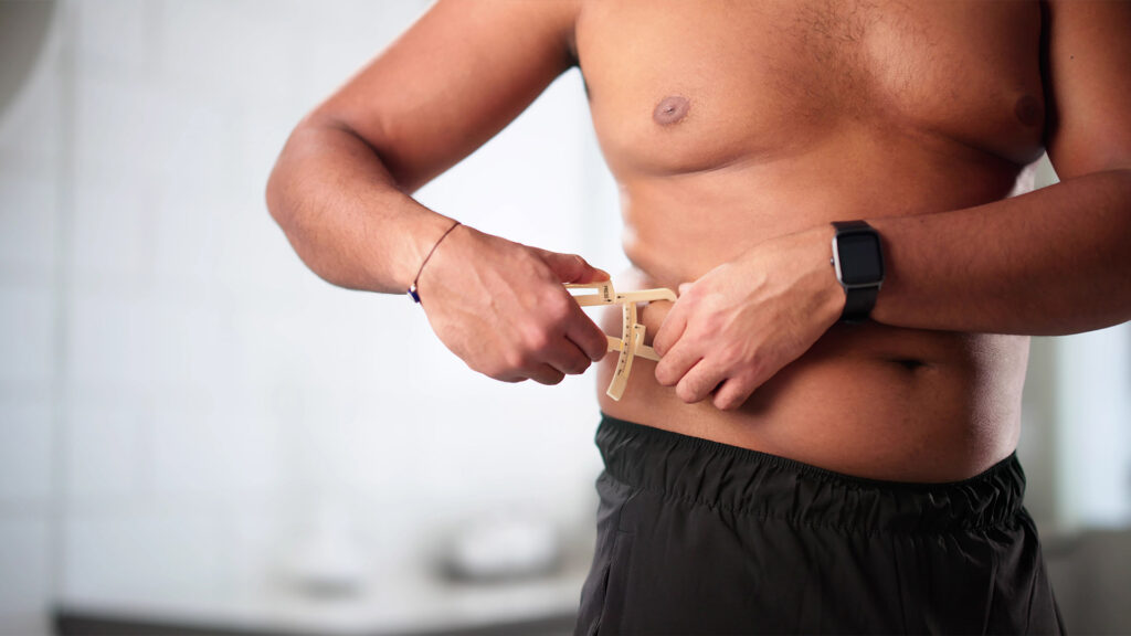 Man measuring abdominal fat with a skinfold caliper at his waist
