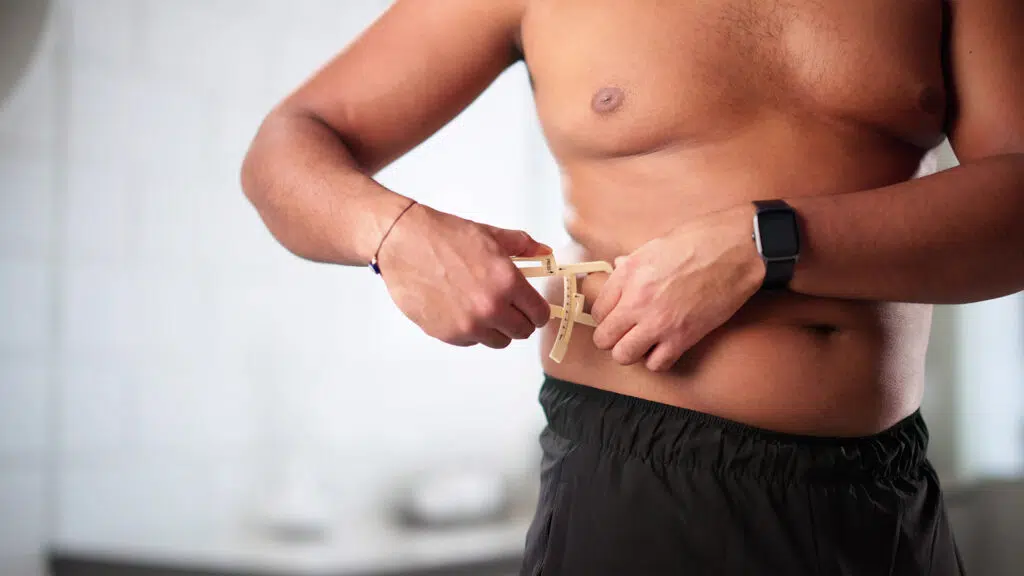 Man measuring abdominal fat with a skinfold caliper at his waist