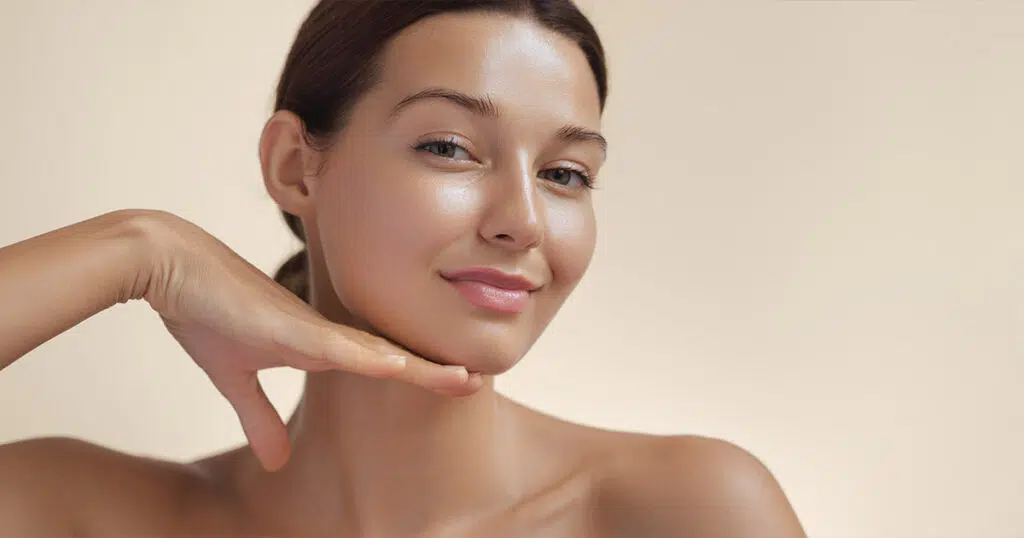 Woman with smooth skin resting her hand beneath her chin against a beige background