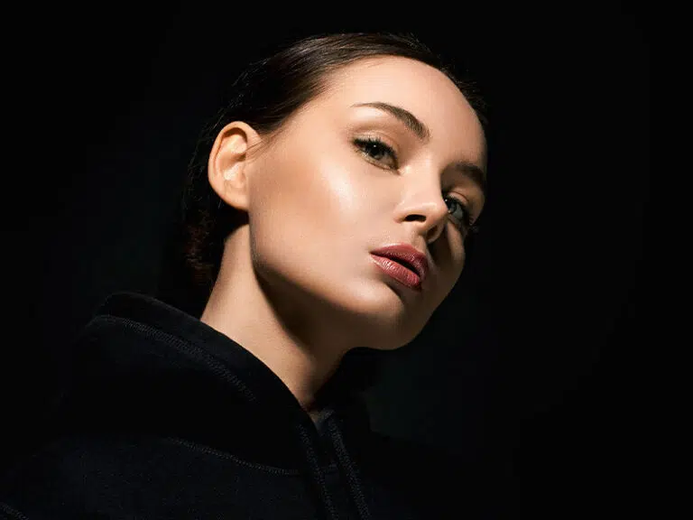 Woman's face in dramatic low-key lighting, head tilted back, highlighting her nose and jawline
