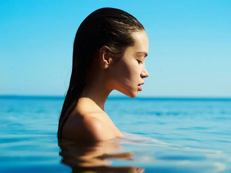 Side profile of a woman with wet hair standing in calm blue water