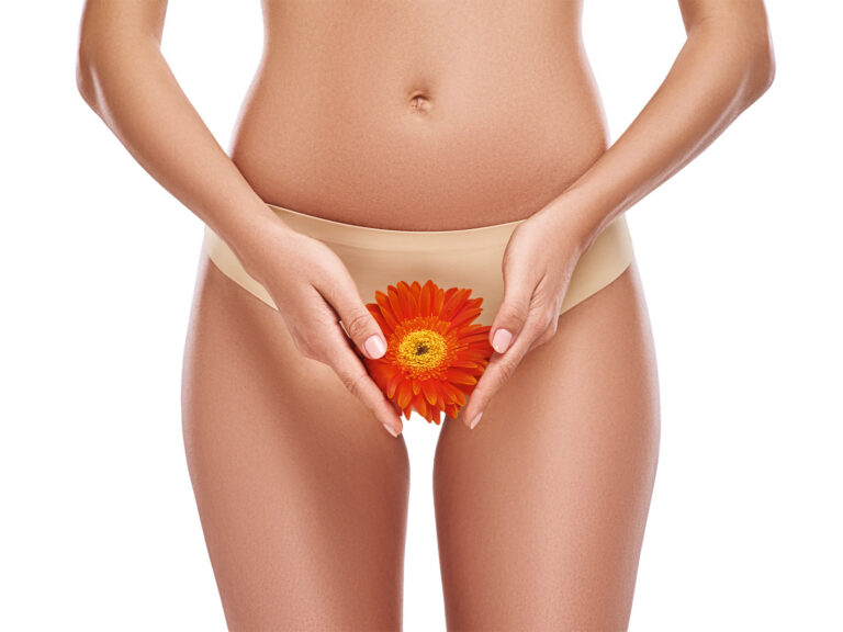 Woman in beige underwear holding an orange gerbera daisy at her pelvic area