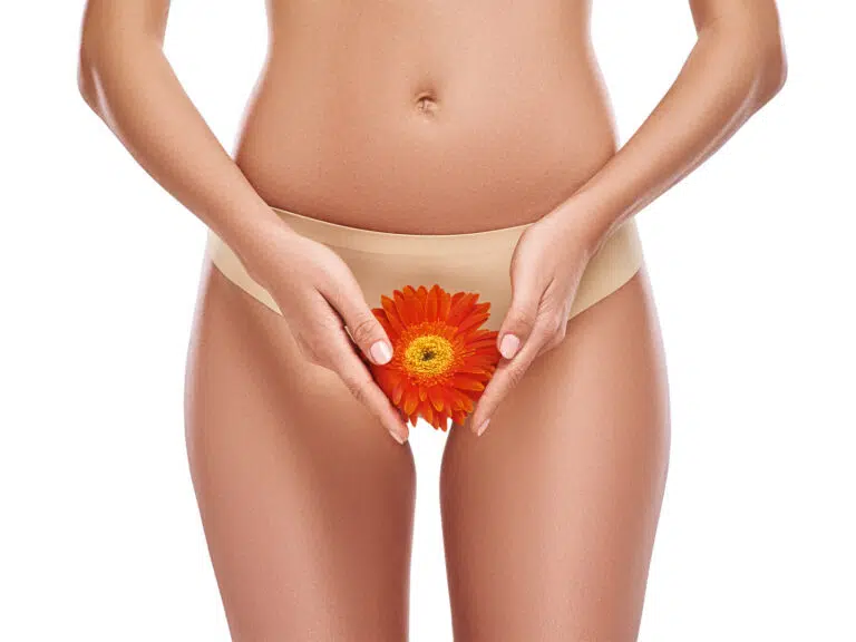 Woman in beige underwear holding an orange gerbera daisy at her pelvic area