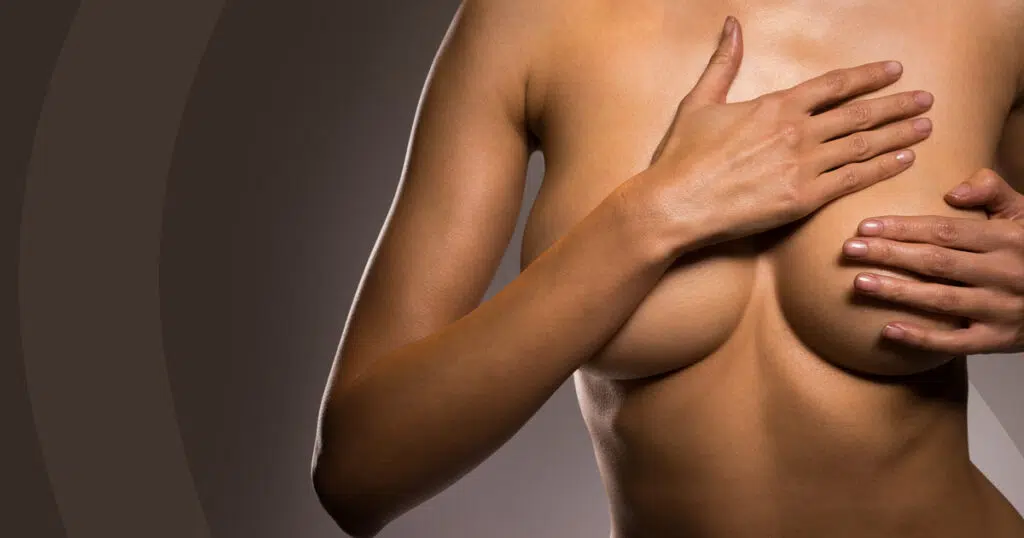 Woman holding her breasts with both hands against a gray background, illustrating breast implant displacement
